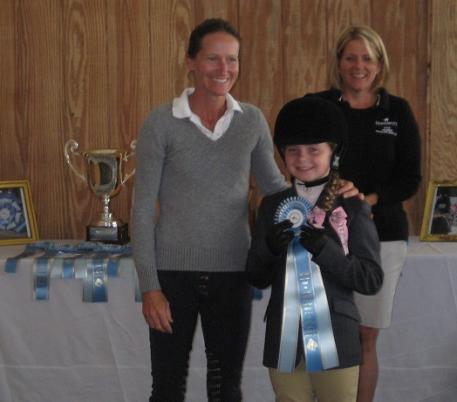 Emily McGowan (center) receives her equitation blue ribbon from grand prix rider Molly Ashe-Cawley (left) as mother Katie McGowan watches.