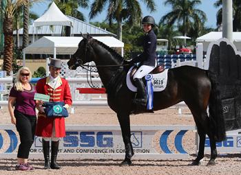 Alexandra Crown, mounted on Von Cim, receives her second ,000 bonus from SSG Gloves representative Jennifer Ward so far this season for wearing SSG ‘Digital’ riding gloves on her way to victory in the 5,000 SJHOF High Amateur-Owner Jumper Classic at the Winter Equestrian Festival in Wellington, FL. Photo by Sportfot